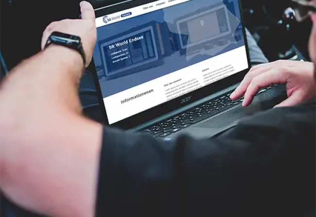 A guy sitting in the driver's seat of a car with a laptop on his lap. A website can be seen on the screen.